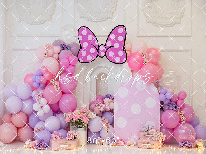 Polka dot bow birthday backdrop with pastel balloon arch and floral accents