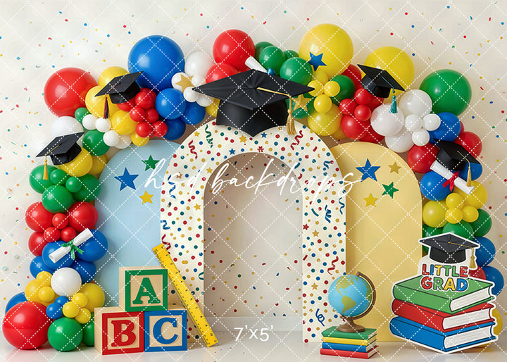 Little grad balloon arch photography backdrop with colorful balloons, graduation caps, ABC blocks, books, and school-themed decor for kids graduation portraits.