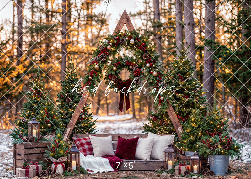 Woodland Christmas A-Frame photography backdrop featuring a rustic wooden triangular arch decorated with lush evergreen garlands, red berries, pinecones, and ornaments, surrounded by glowing Christmas trees, a cozy wooden bench with plaid pillows, ivory blankets, lanterns, and warm golden woodland scenery for holiday portraits.