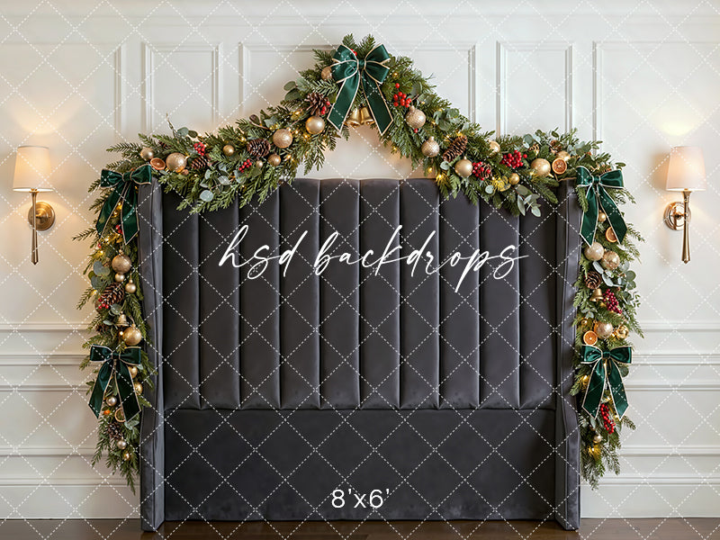 Winter Manor Headboard photography backdrop with a dark upholstered headboard, festive garland, emerald velvet bows, glowing lights, and elegant Christmas décor for portrait photography.