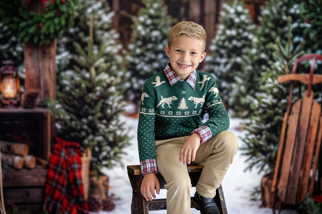 Rustic Christmas tree farm portrait backdrop with snowy pine trees, wooden farm details, red plaid holiday accents, warm lanterns, sleds, and festive winter studio styling.