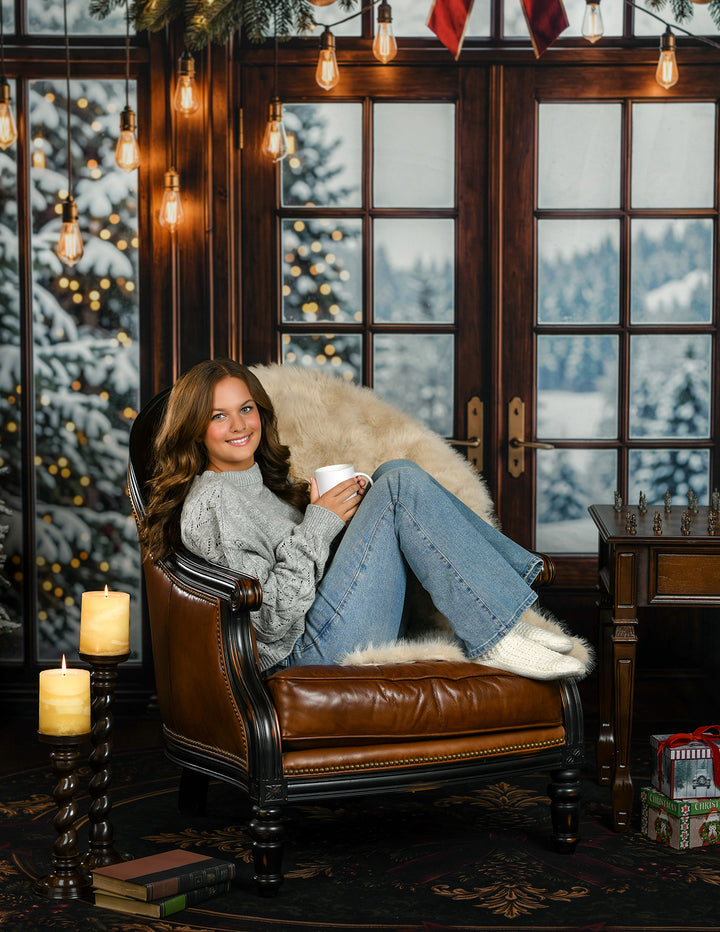 Cozy winter window Christmas photography backdrop with dark wood French doors, snowy evergreen view, warm hanging lights, holiday garland, candles, leather chair, and classic winter portrait styling.