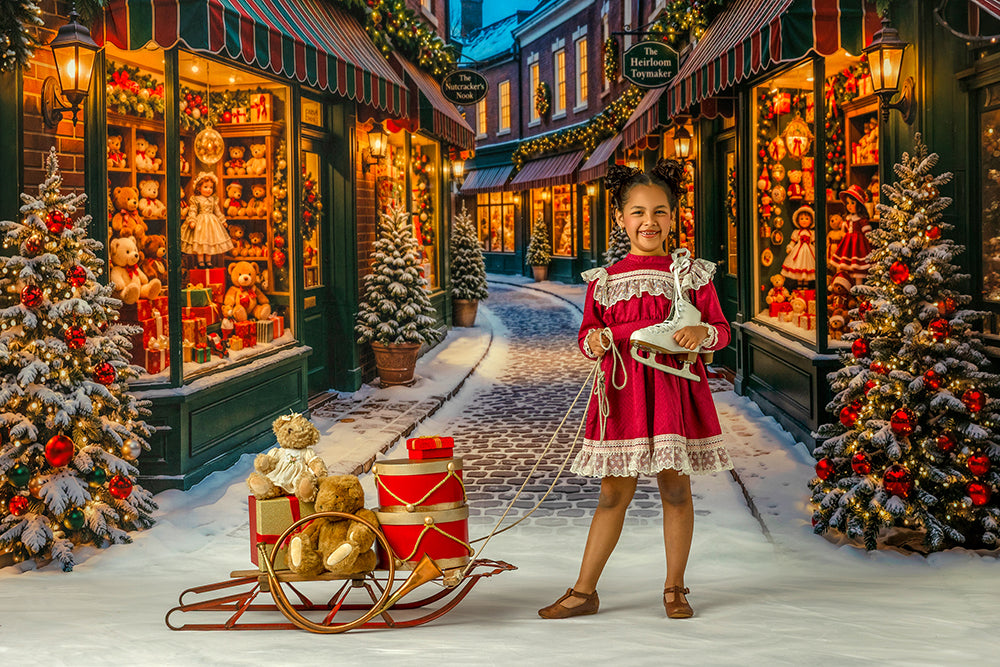 Christmas toy shop street photography backdrop with snowy cobblestone road, glowing holiday storefronts, decorated Christmas trees, teddy bears, wrapped gifts, and festive village styling.