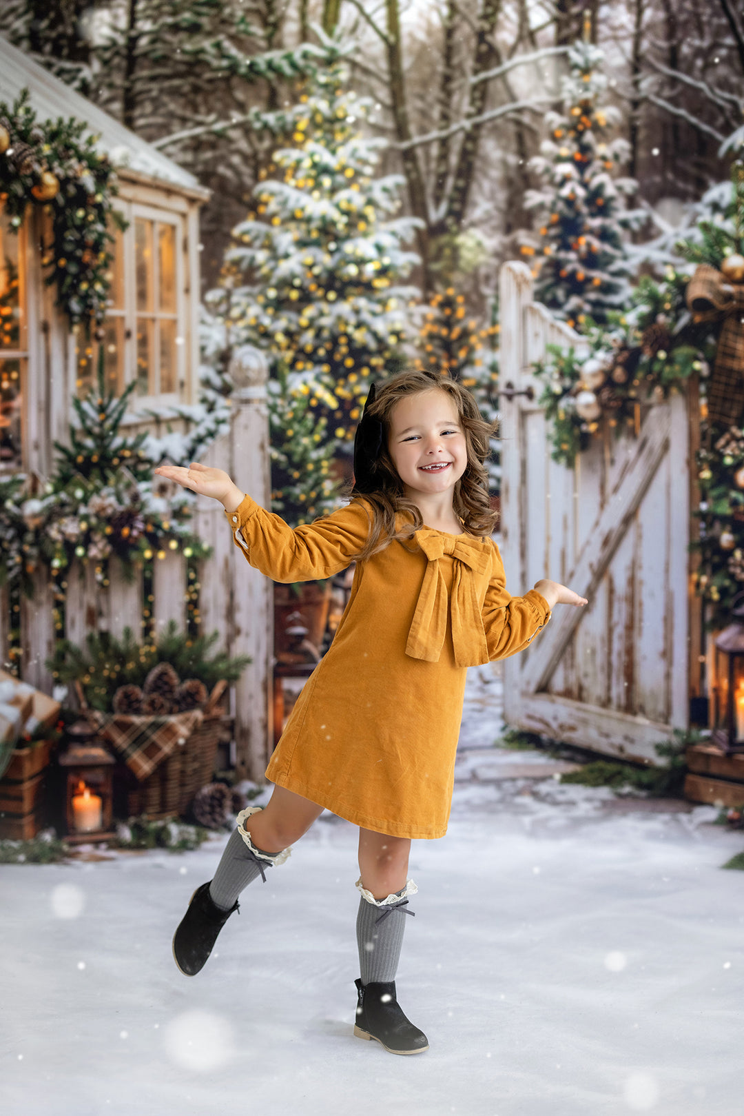 Cozy winter cottage garden photography backdrop with snowy trees, glowing Christmas lights, greenhouse windows, rustic white gate, evergreen décor, and warm holiday styling.