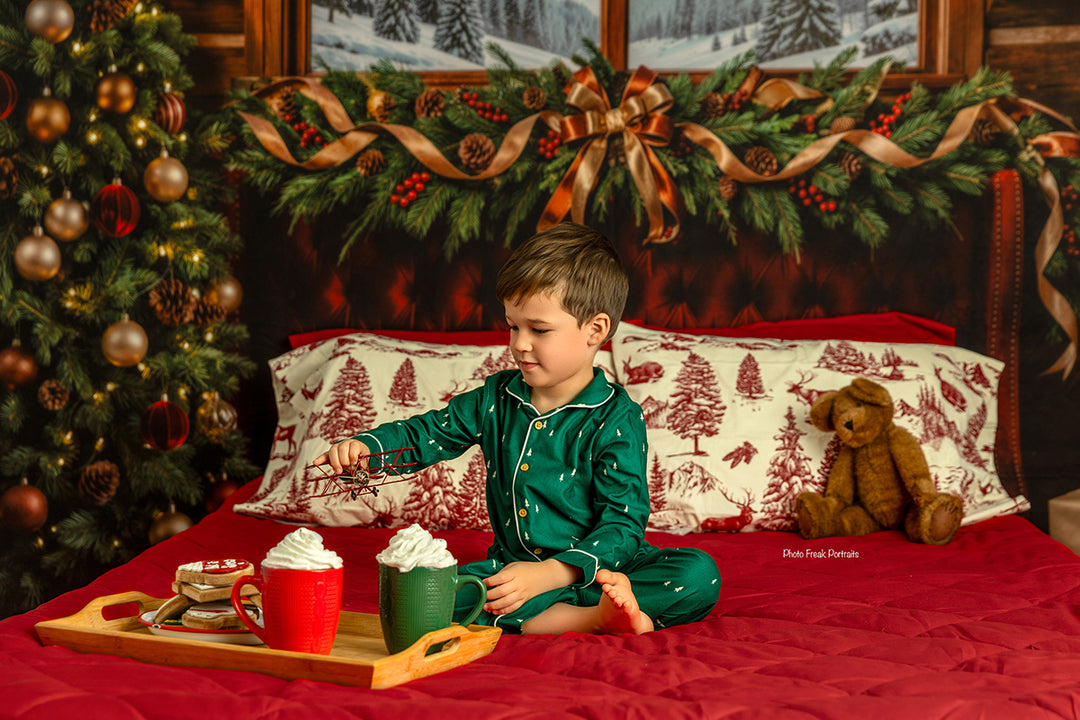 Rustic winter lodge Christmas backdrop with mountain window scene, cabin wood walls, burgundy bed, evergreen garland, holiday pillows, Christmas tree, and cozy winter portrait details.
