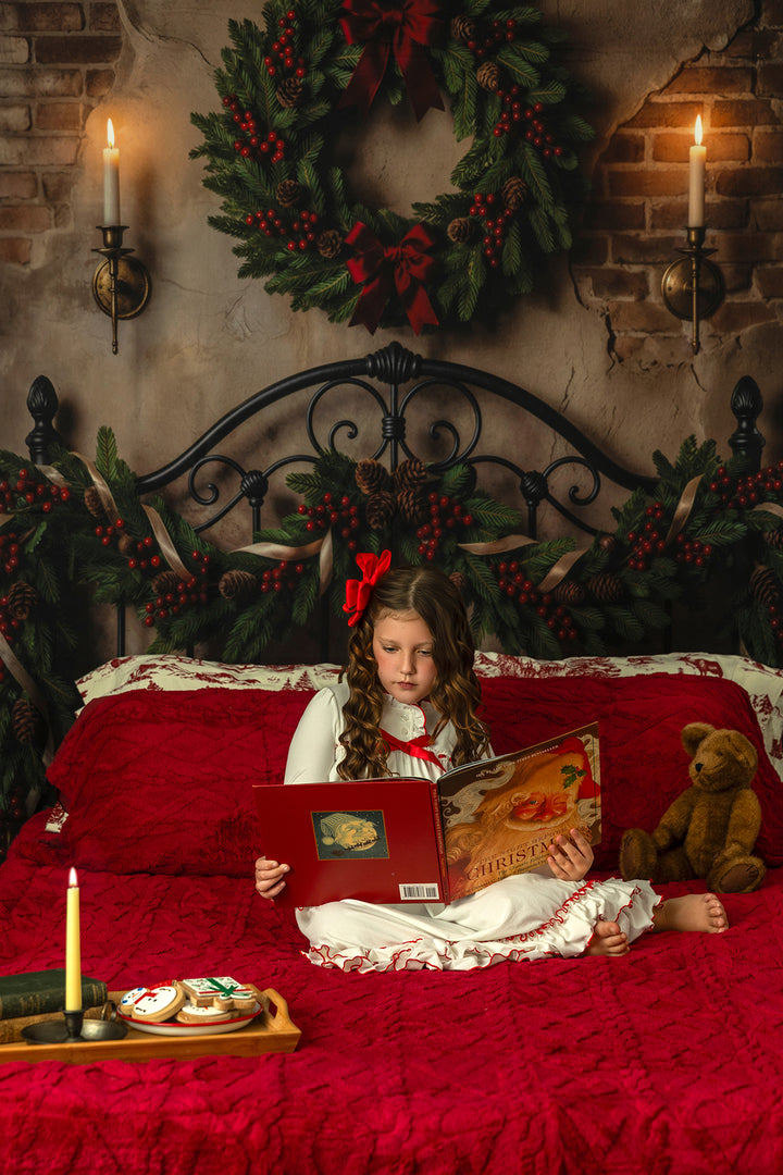 Christmas bedframe pajama mini backdrop with festive greenery, red blanket, snowy window views, candlelight, lanterns, pinecones, berries, and warm winter holiday décor.