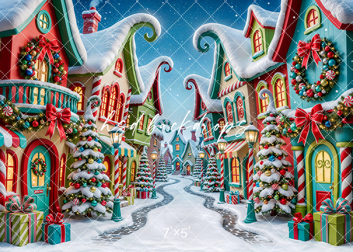 Merryville Christmas Village photography backdrop with colorful snowy buildings, candy-inspired details, decorated Christmas trees, glowing windows, festive wreaths, wrapped gifts, peppermint accents, and whimsical holiday street styling.