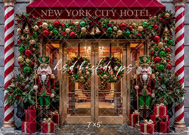 New York City Hotel Christmas photography backdrop with red hotel awning, glowing lobby doors, nutcracker soldiers, candy cane columns, evergreen garland, wreaths, red and green ornaments, wrapped gifts, and festive holiday entrance styling.