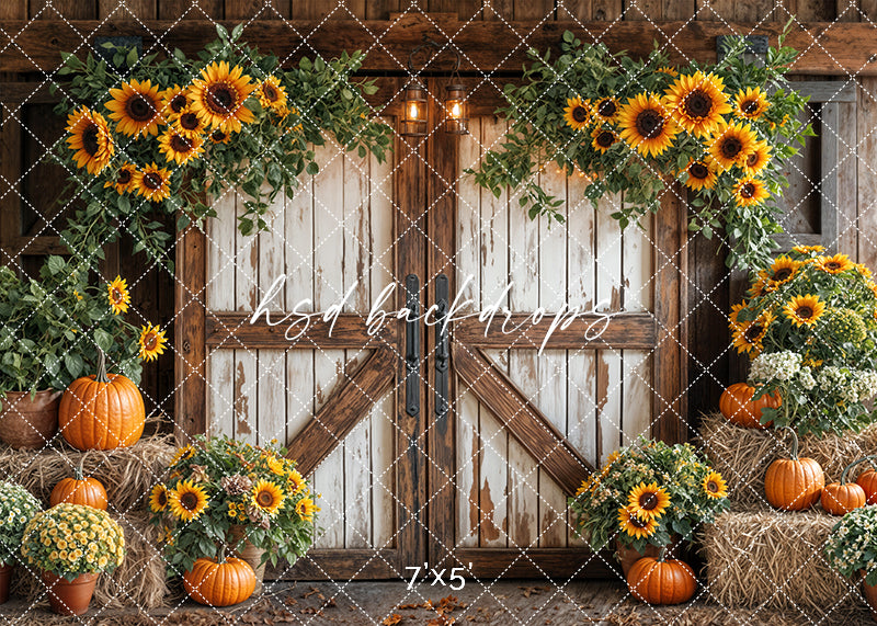 Fall photography backdrop with rustic barn doors, hanging sunflowers, hay bales, orange pumpkins, and potted yellow mums.