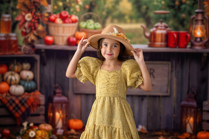 Rustic apple orchard cider stand backdrop with warm fall leaves, apple baskets, pumpkins, glowing lanterns, wooden booth, and cozy autumn market details.