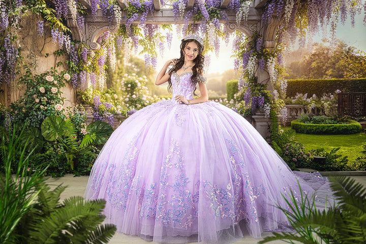 Lavender wisteria garden quinceañera photography backdrop featuring a young woman in a sparkling lilac ball gown beneath an ornate stone pergola with cascading purple and white wisteria.