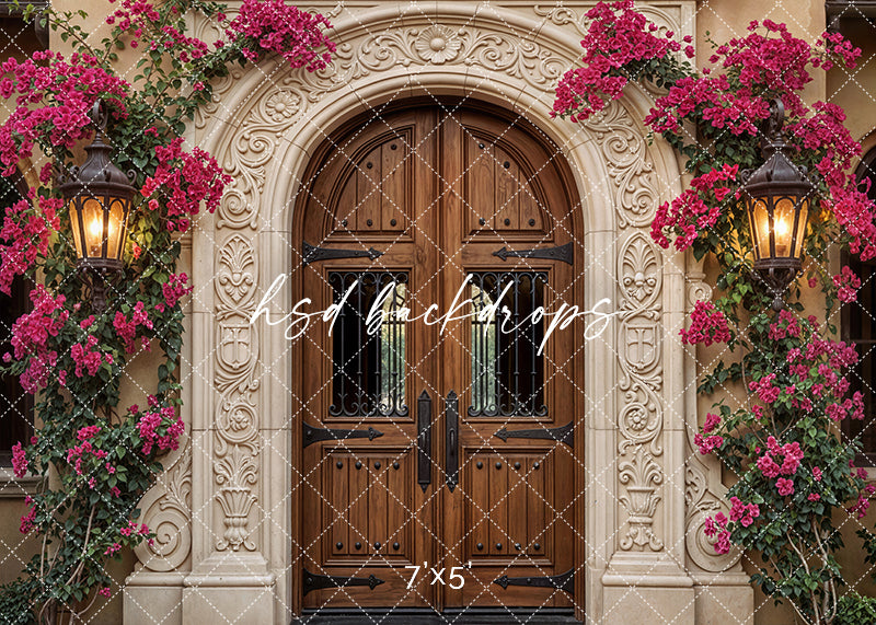 Spanish-style photography backdrop with carved stone archway, wooden double doors, glowing lanterns, and vibrant bougainvillea vines.