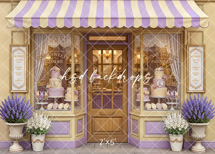 Pastel Easter bakery backdrop with lavender and cream patisserie storefront, cakes, and spring décor for photo sessions