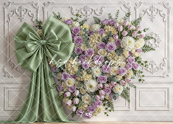 Sage and lavender floral heart wall with roses, tulips, greenery, and a sage satin bow in an elegant studio setting.