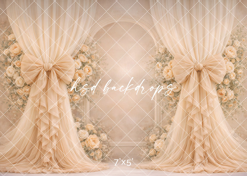 Champagne rose bow photography backdrop with elegant neutral drapery and floral arch for romantic portrait sessions.
