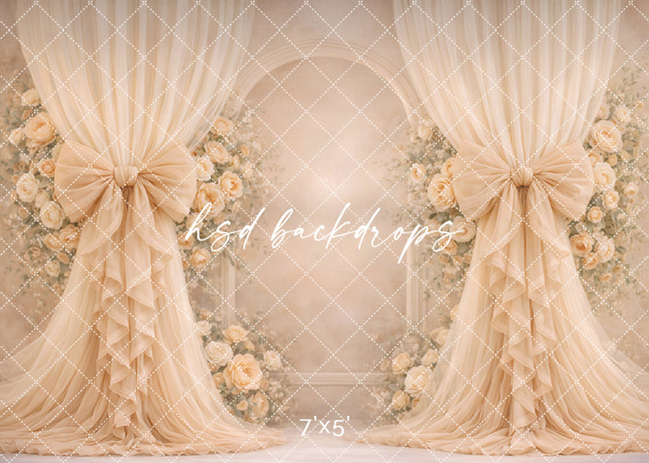 Champagne rose bow photography backdrop with elegant neutral drapery and floral arch for romantic portrait sessions.