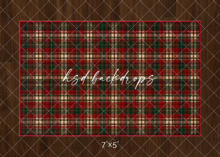 Tartan Christmas rug photography backdrop with classic red, green, cream, and black plaid pattern on a warm wood floor for cozy holiday studio portraits.