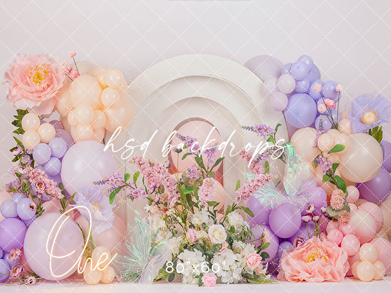 Pastel One Wildflower photography backdrop with layered arches, pastel pink and lavender balloons, florals, butterfly accents, and a glowing one sign for girls birthday portraits.