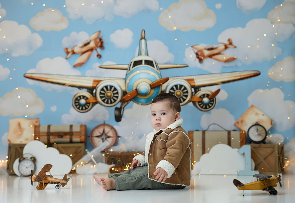 Vintage Airplane Adventure photography backdrop with a large airplane, fluffy clouds, travel trunks, maps, clocks, and sky-themed birthday details for boys portraits.