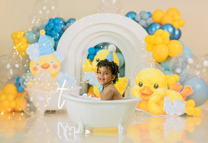 Rubber Ducky Birthday photography backdrop with yellow duck accents, blue and yellow balloons, bubbles, layered arches, and playful bath time styling for boys birthday portraits.