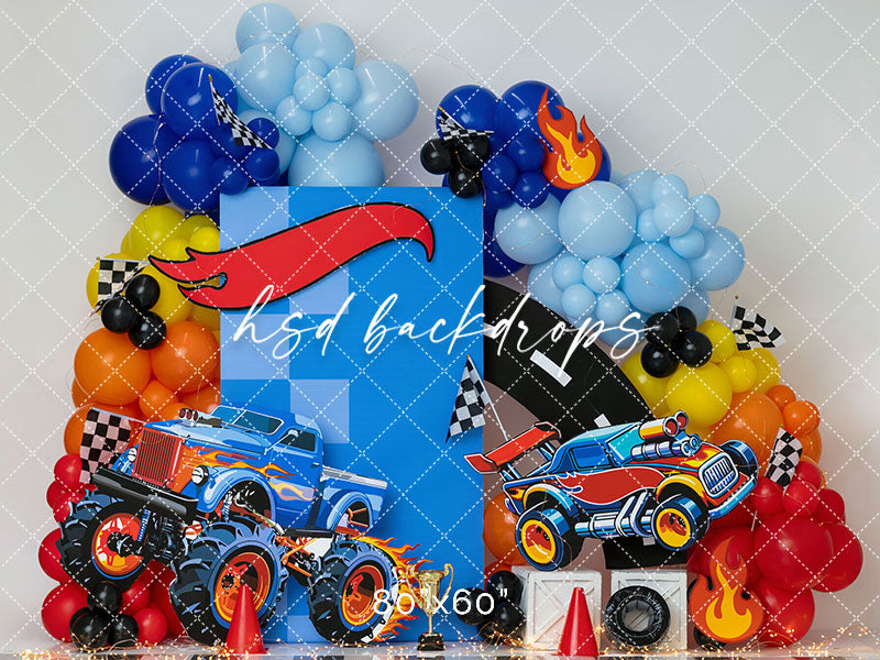 Monster Truck Birthday photography backdrop with colorful balloon garlands, monster truck graphics, checkered flags, racing flames, traffic cones, and cake smash birthday styling.