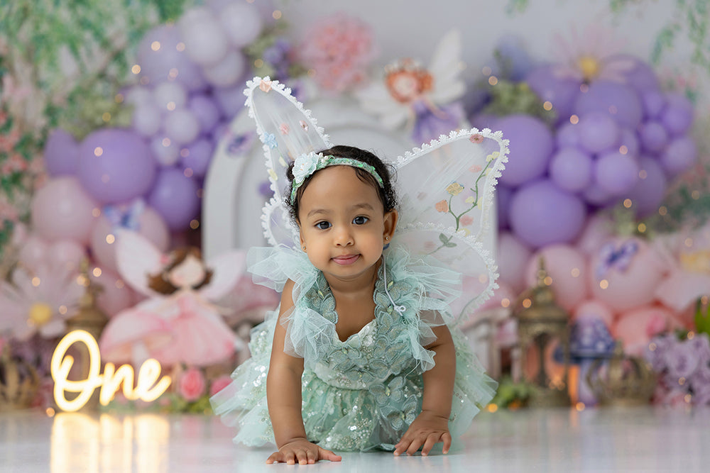 Fairies & Flowers cake smash backdrop with pastel balloon garlands, fairy garden details, flowers, mushrooms, butterflies, lanterns, greenery, and enchanted birthday styling.