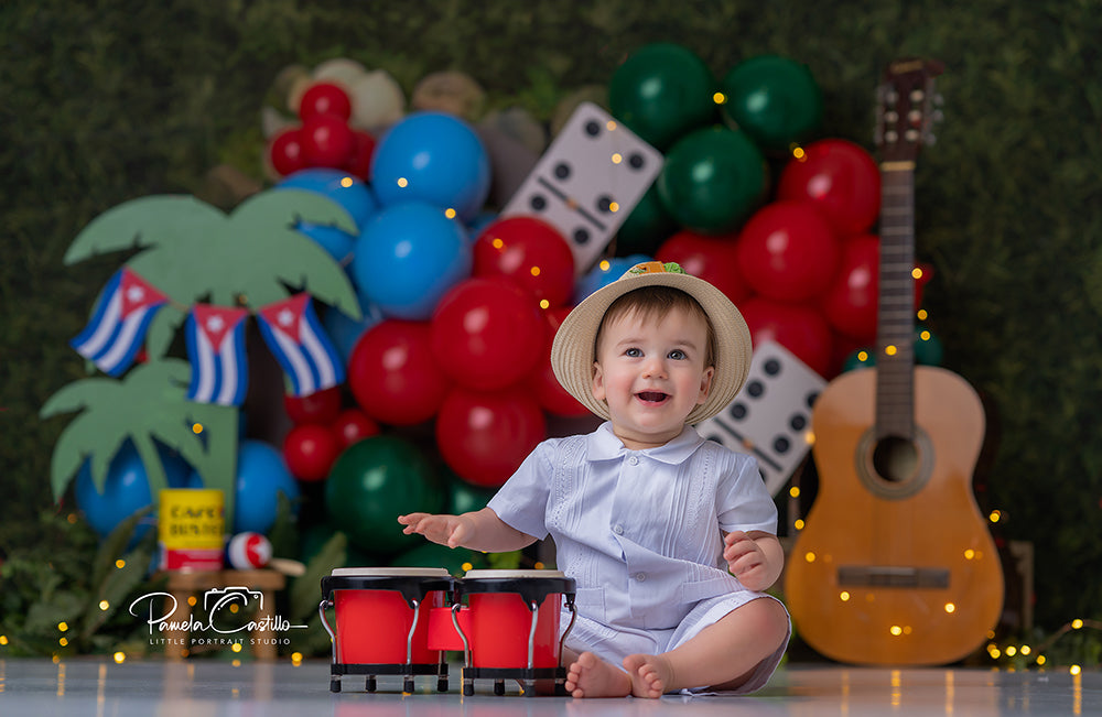 Havana Domino Party photography backdrop with red, blue, green, and black balloon garlands, oversized dominoes, tropical palm accents, Cuban-inspired flags, café props, greenery, and classic guitar.
