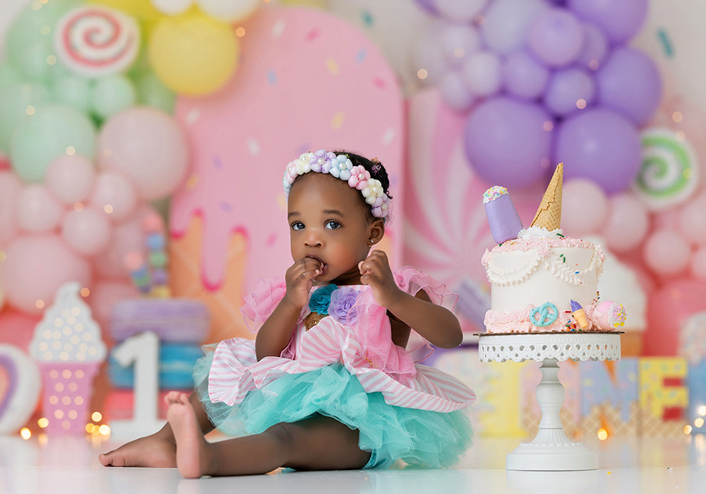 Sprinkle Wishes cake smash backdrop with pastel balloon garlands, sprinkle wall, oversized ice cream treats, lollipops, macarons, candy accents, and sweet pastel birthday styling.