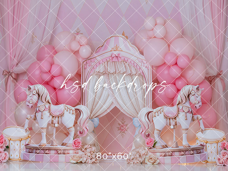 Harlequin Royale Carousel cake smash backdrop with pink balloon garlands, white carousel horses, blush drapery, harlequin diamond wall details, floral accents, drum props, and elegant birthday studio styling.
