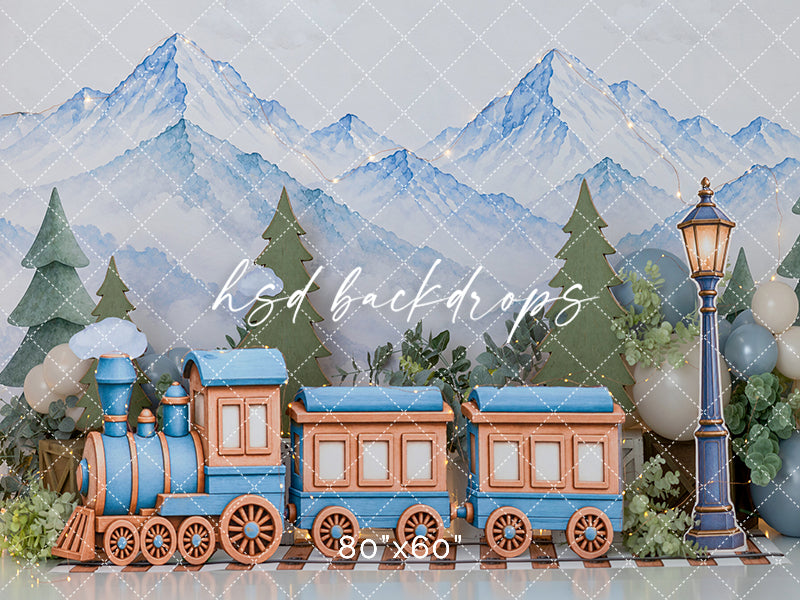 Winter mountain train photography backdrop with a charming blue locomotive, copper passenger cars, watercolor alpine mountains, evergreen trees, and soft winter greenery.