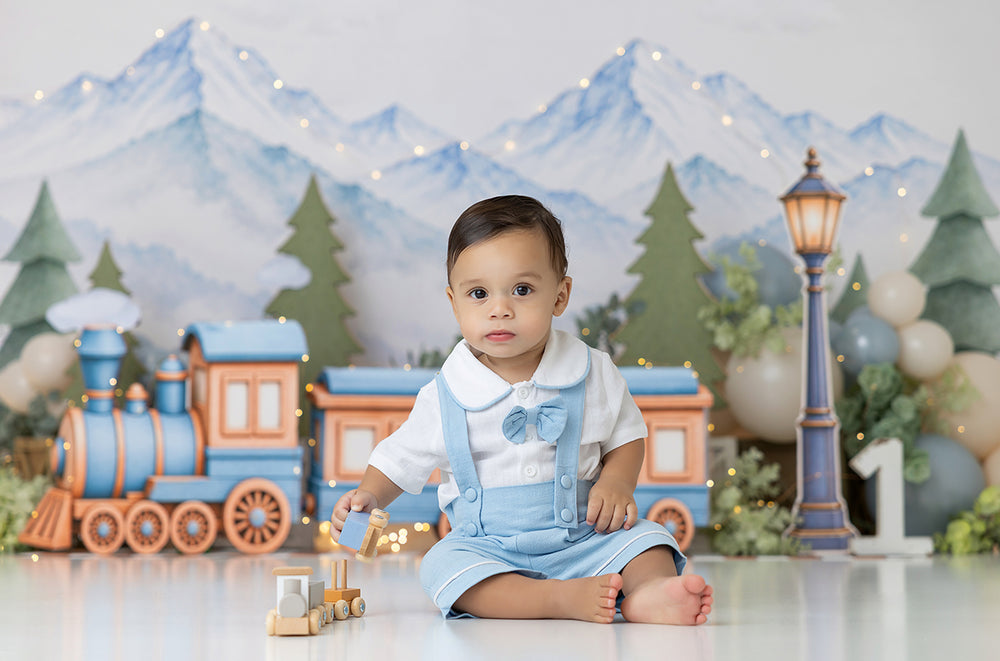 Alpine Adventure Train photography backdrop featuring a vintage blue and copper toy train with coordinating passenger cars, watercolor snowy alpine mountains, evergreen trees, pastel blue and ivory balloons, soft greenery, and a glowing blue streetlamp for whimsical winter portraits.