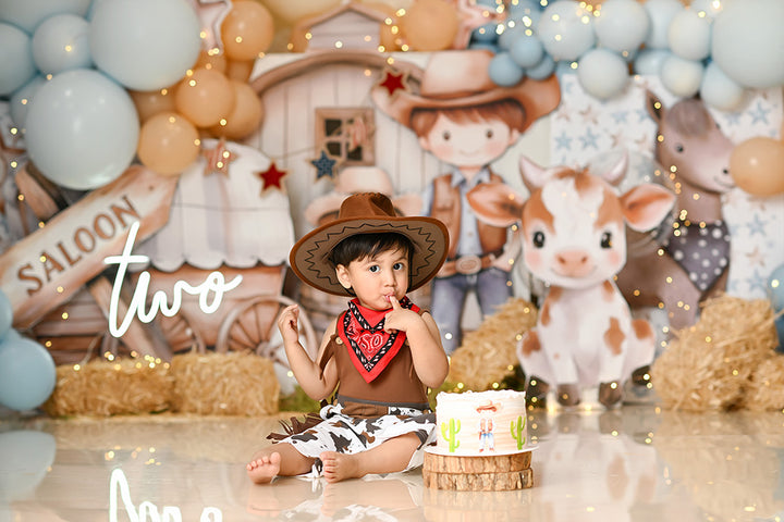 Western cowboy-themed cake smash backdrop with calf, wagon, balloons, and hay for first birthday portraits