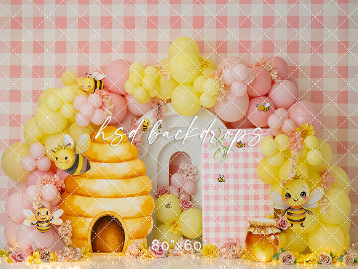 Bee-themed photo backdrop with yellow beehive, pastel balloons, honey jar, and gingham pattern – Golden Honey Bee Hive design by HSD Backdrops.