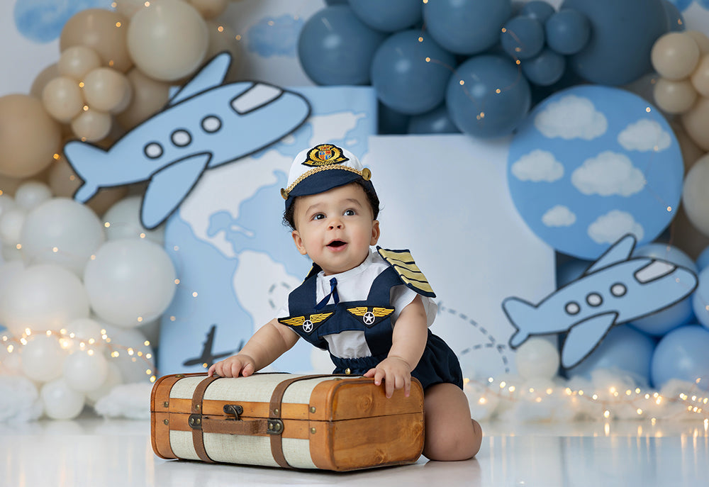 Airplane-themed photo backdrop with pastel balloons, clouds, world map, and two cartoon planes – Miles of Smiles design by HSD Backdrops.