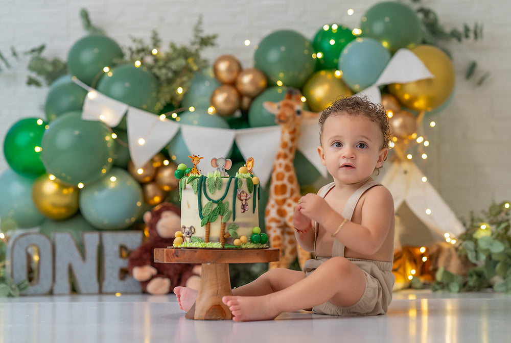 Safari-themed birthday photography backdrop with jungle balloons, teepee, and stuffed animals.