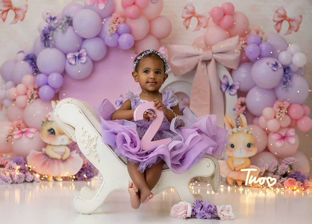 Butterfly Kisses and Bows pink and lavender photography backdrop with butterflies, bows, and floral balloon garland for birthday and cake smash photoshoots.
