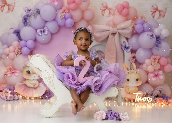 Butterfly Kisses and Bows pink and lavender photography backdrop with butterflies, bows, and floral balloon garland for birthday and cake smash photoshoots.