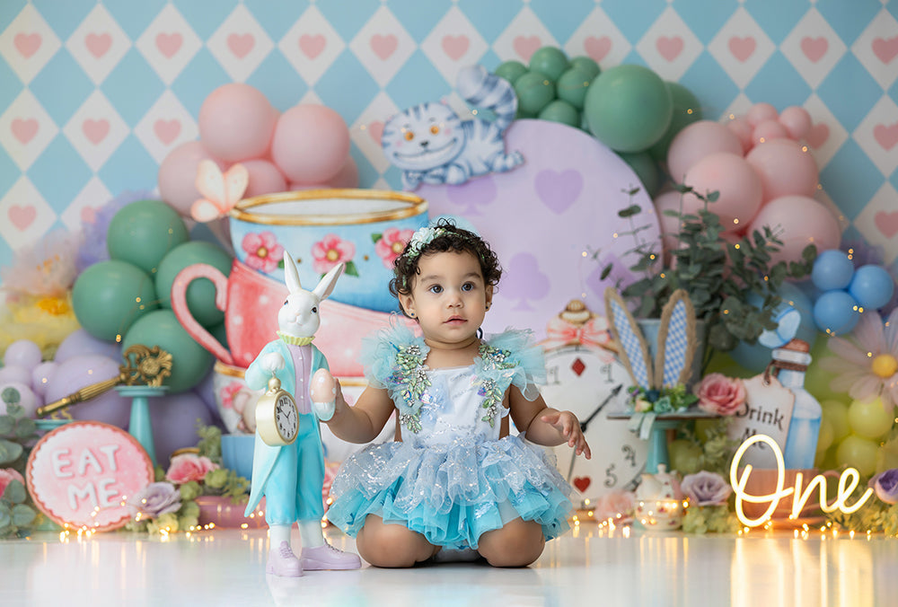 Mad Hatter’s Tea Party Alice in Wonderland photography backdrop with stacked teacups, clock, Cheshire Cat, and pastel balloon setup for birthday or cake smash photoshoots.