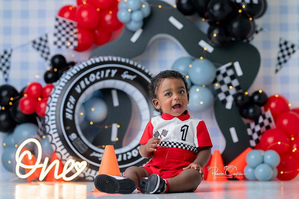 Pit Stop Party race car cake smash backdrop with checkered flags, tire props, cones, and road track design for racing-themed photoshoots.