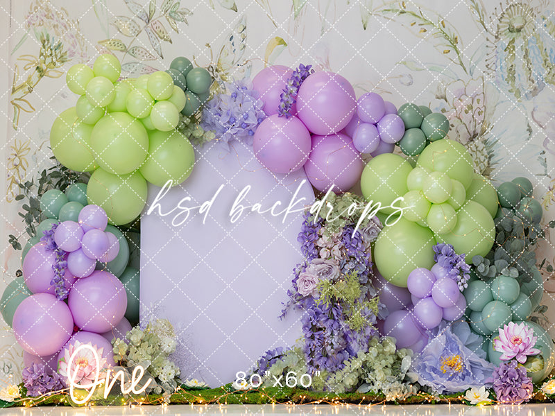 Pastel first birthday backdrop with whimsical balloon arch, florals, and soft garden-inspired colors