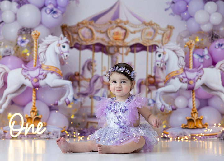 Lilac and Gold Carousel backdrop with whimsical carousel horses, pastel balloons, and fairytale birthday photo setup.