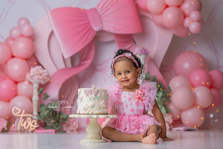 ink Bow Party girly birthday cake smash backdrop with blush balloons and oversized pink bow.