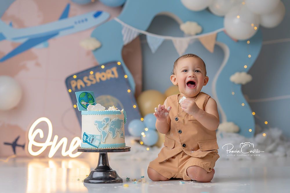 Travel-themed airplane cake smash backdrop with passport and balloons