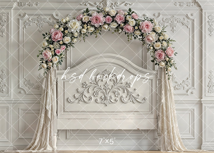 Elegant ivory headboard with ornate detailing and a blush and cream rose floral arch, framed by draped fabric, for luxury princess and portrait photography.