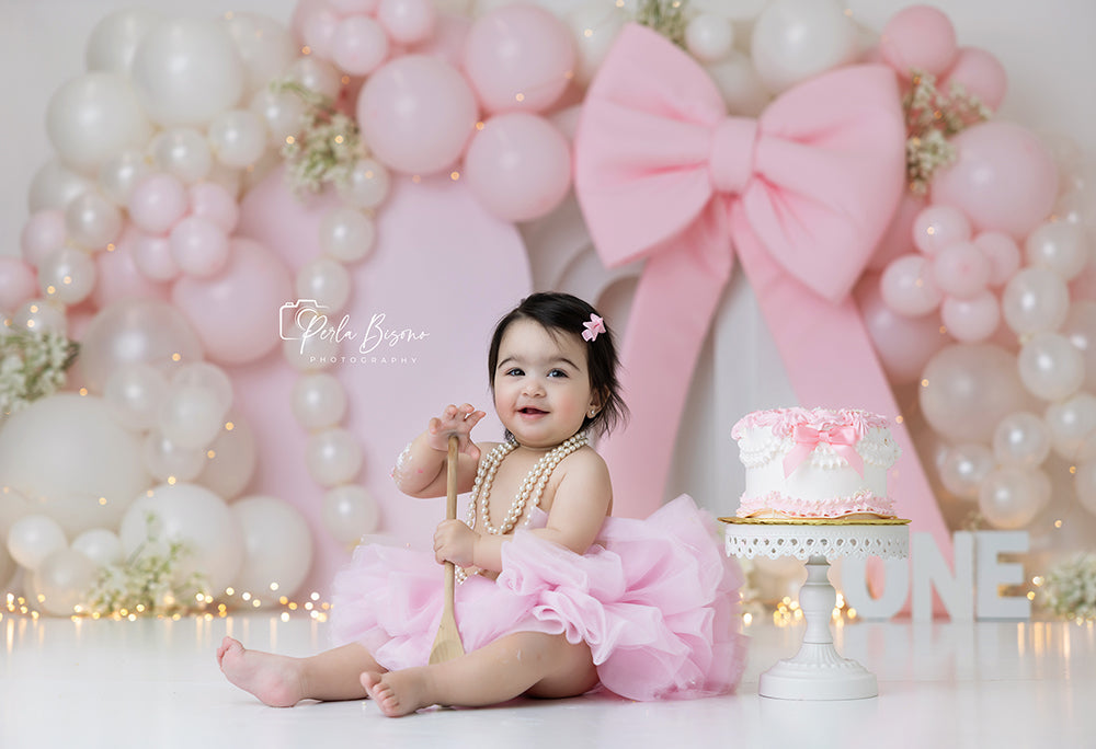Pearl luxe baby pink balloon arch cake smash photography backdrop with elegant bow for girl first birthday portraits.