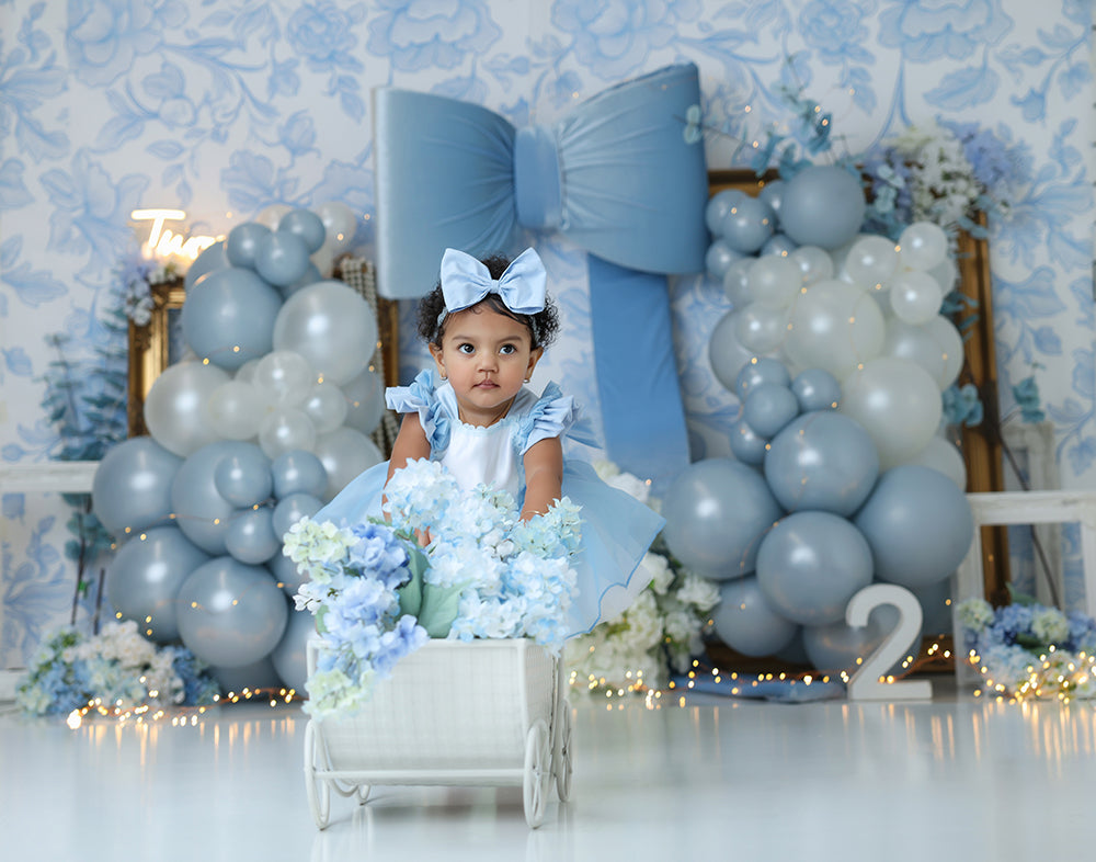 Blue bow balloon cake smash photography backdrop with baby blue balloons, oversized bow, and floral accents for first birthday sessions.