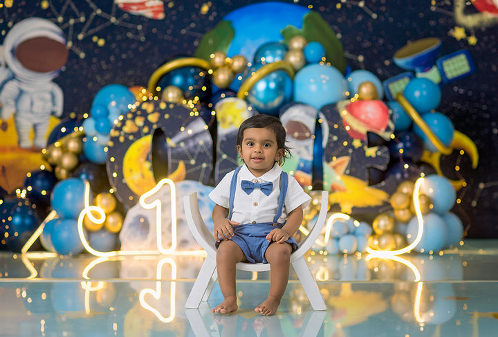 One in Space boys cake smash photography backdrop with astronaut, planets, rockets, and blue balloon clusters for first birthday sessions.