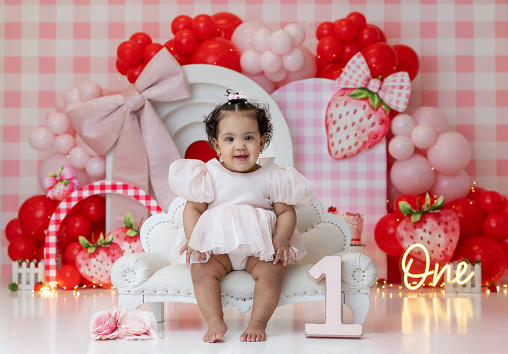 Berry Berry Sweet strawberry cake smash photography backdrop with pink arches, red and blush balloons, oversized strawberries, bows, and gingham details for girls birthday portraits.